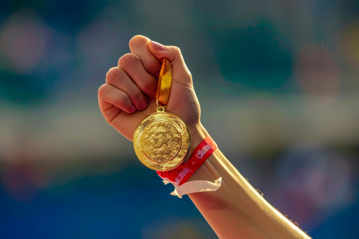hand of a woman raising an Olympic gold medal in victory